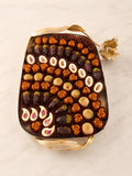 An assortment of chocolate and nut confections arranged in a decorative gold-toned rectangular tray on a light marble surface.