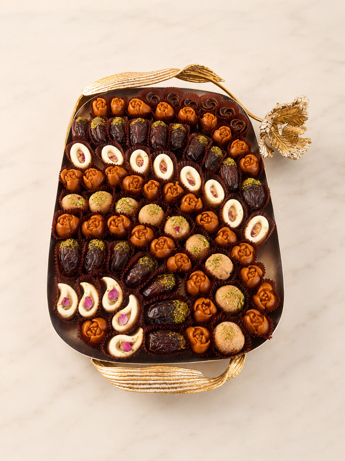 An assortment of chocolate and nut confections arranged in a decorative gold-toned rectangular tray on a light marble surface.