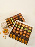 Two boxes of assorted chocolates and bite sized halva sweets on a light wooden surface with small containers of halva.